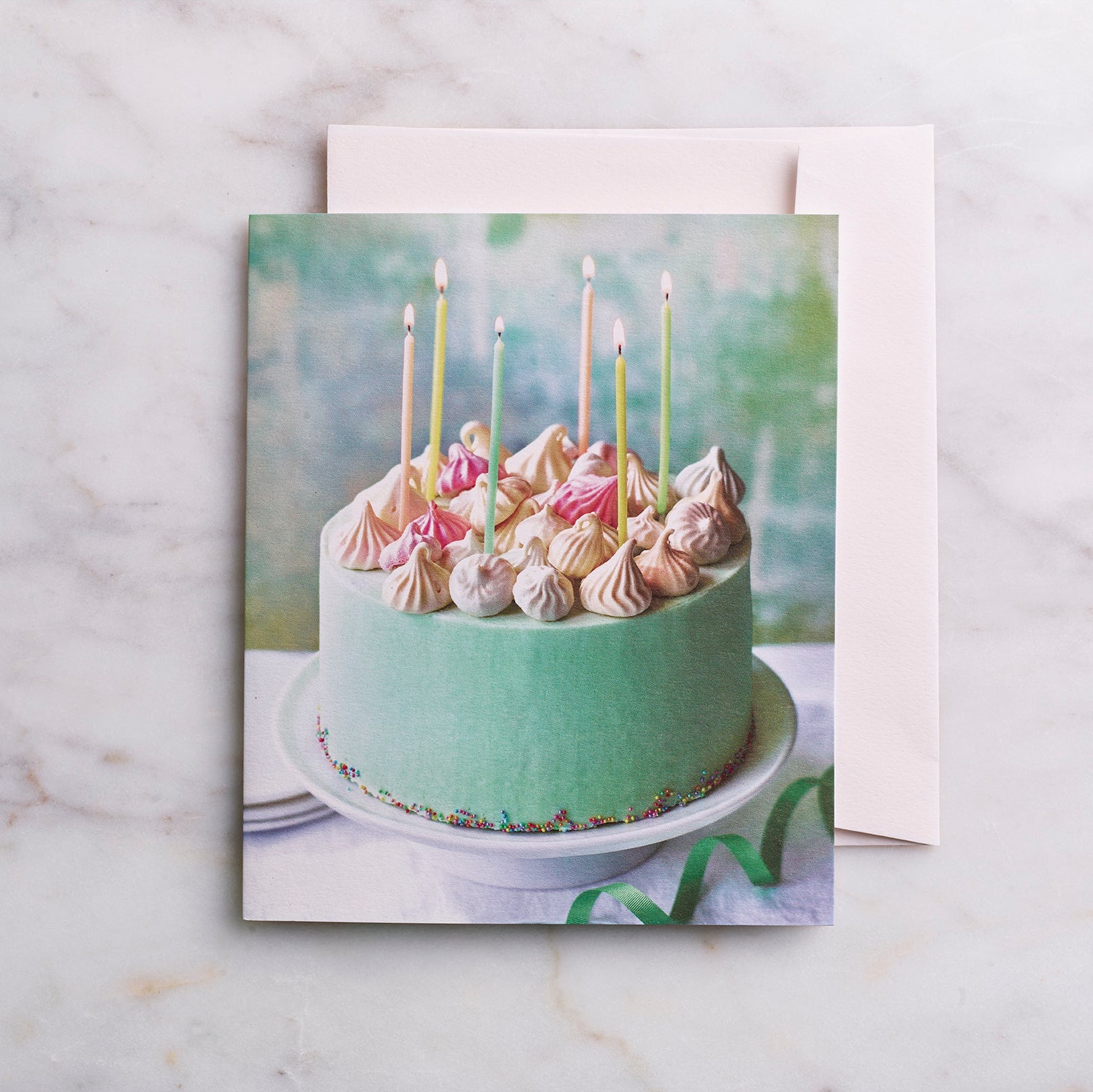 Greeting card with a cake design featuring candles and meringues on a marble surface