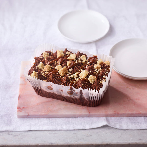 Chocolate loaf cake with crumbly topping on a wooden board with two white plates.