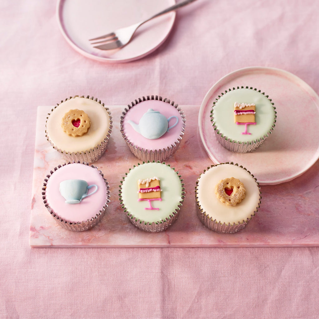 Afternoon Tea Fairy Cakes, six pastel fondant cakes with handcrafted teacup, teapot, cake slice and heart biscuit sugar decorations on a pink board.