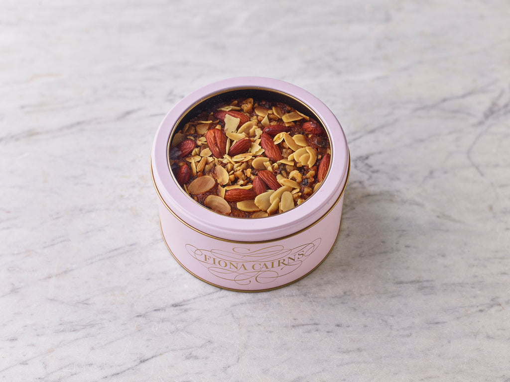 Brandy soaked fruitcake with walnuts and almonds in a pink Fiona Cairns tin on a marble surface.