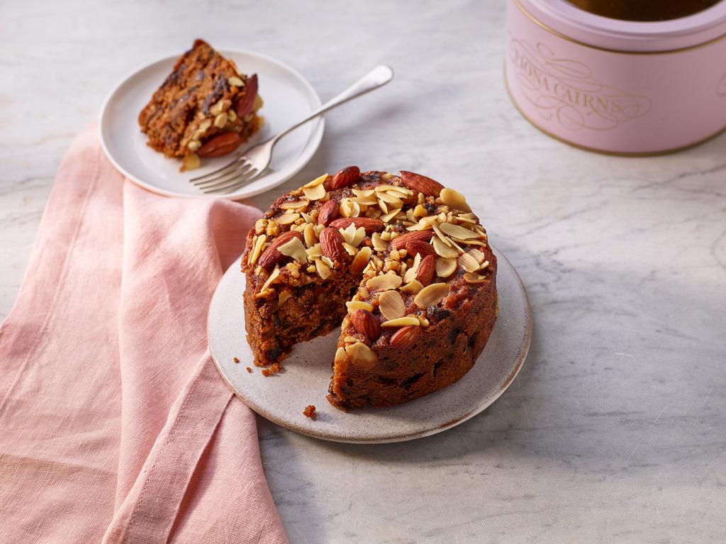 Brandy soaked sliced fruitcake with walnuts and almonds on a plate on a marble surface.