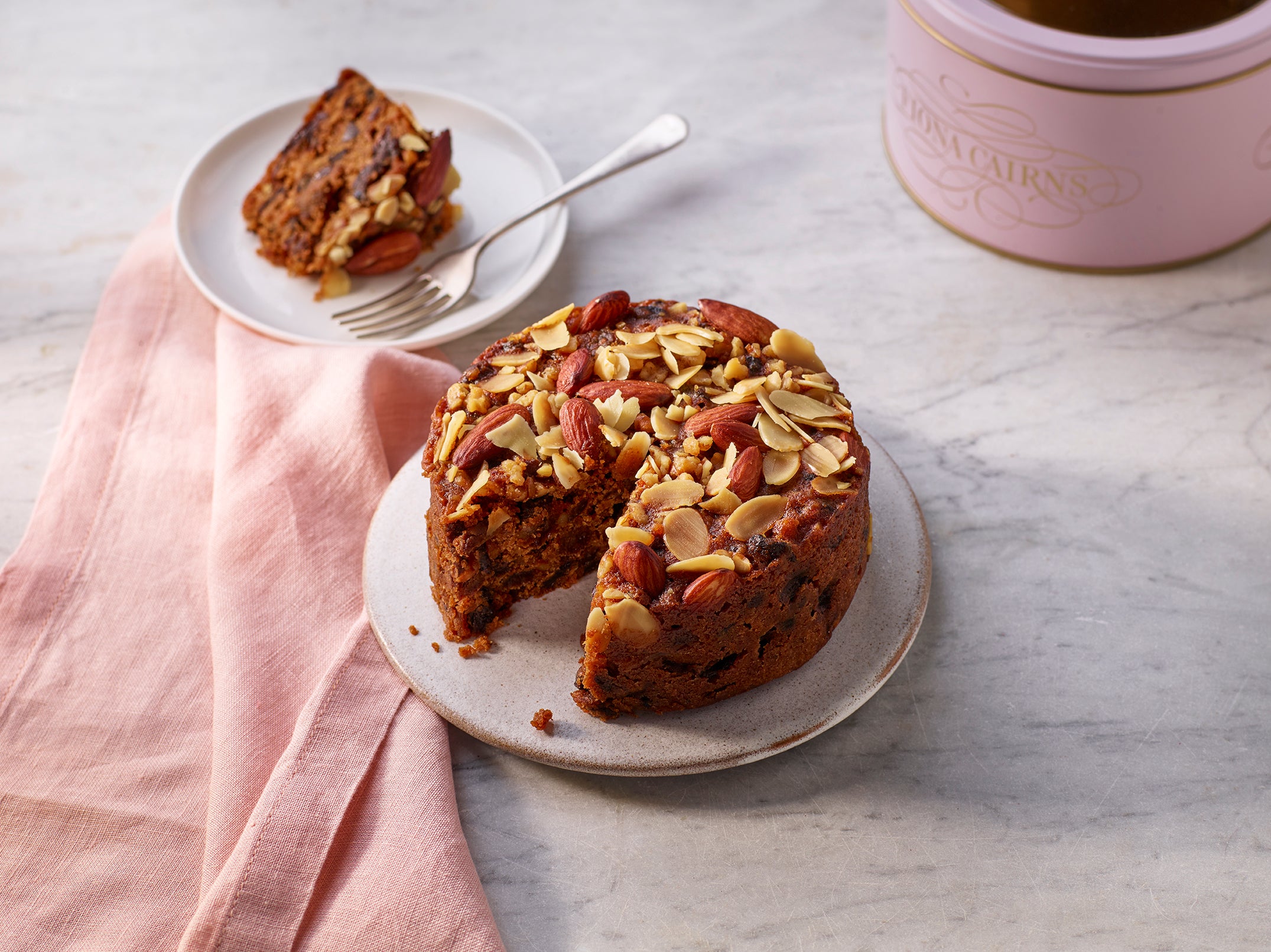 Brandy soaked sliced fruitcake with walnuts and almonds on a plate on a marble surface.