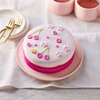 Decorative cake with pink and white design on a white tablecloth with cups and plates.