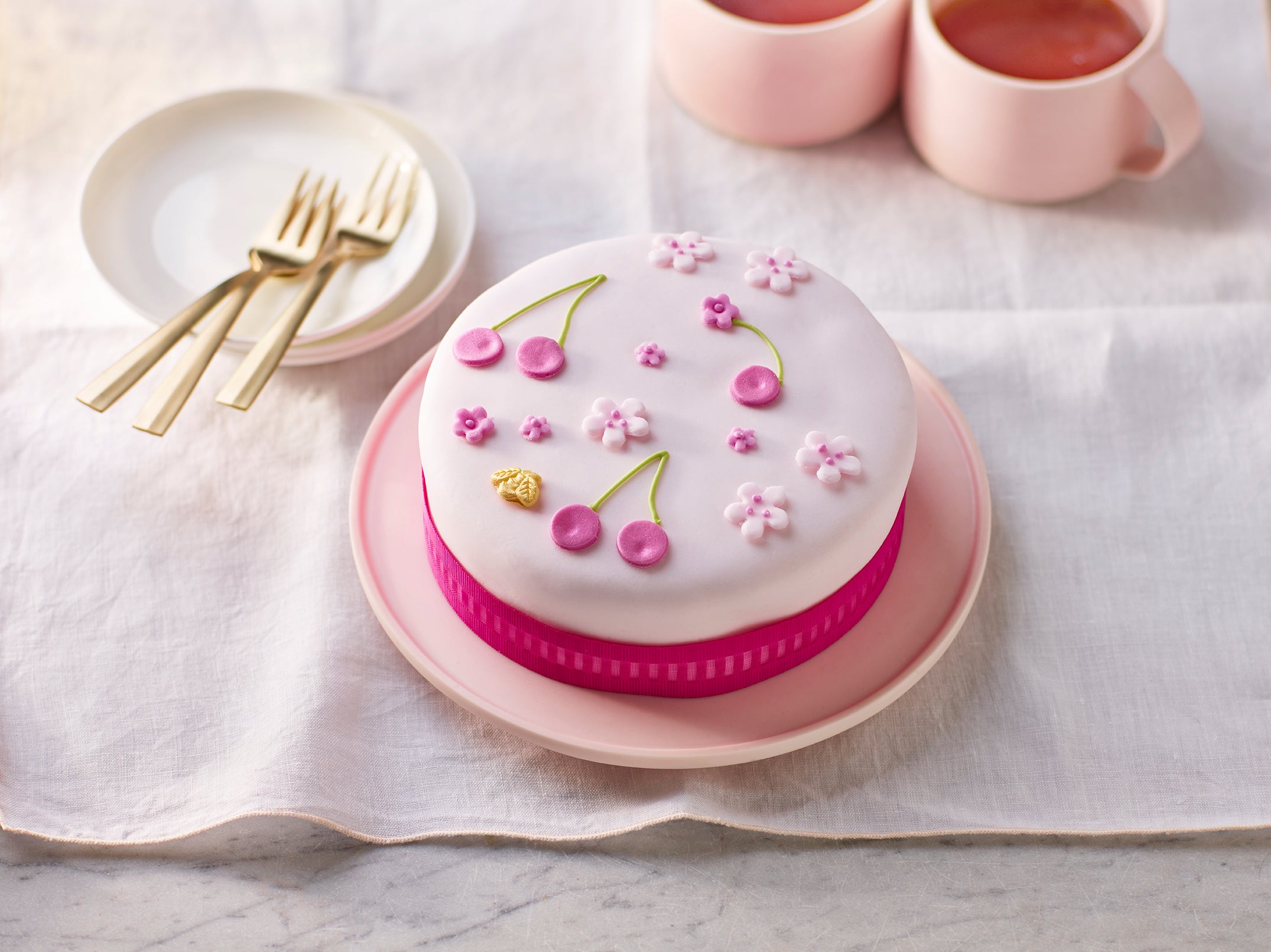 Decorative cake with pink and white design on a white tablecloth with cups and plates.