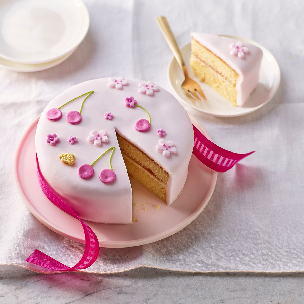 Decorative cake with a slice taken out on a pink plate, surrounded by white plates and a fork on a light background.