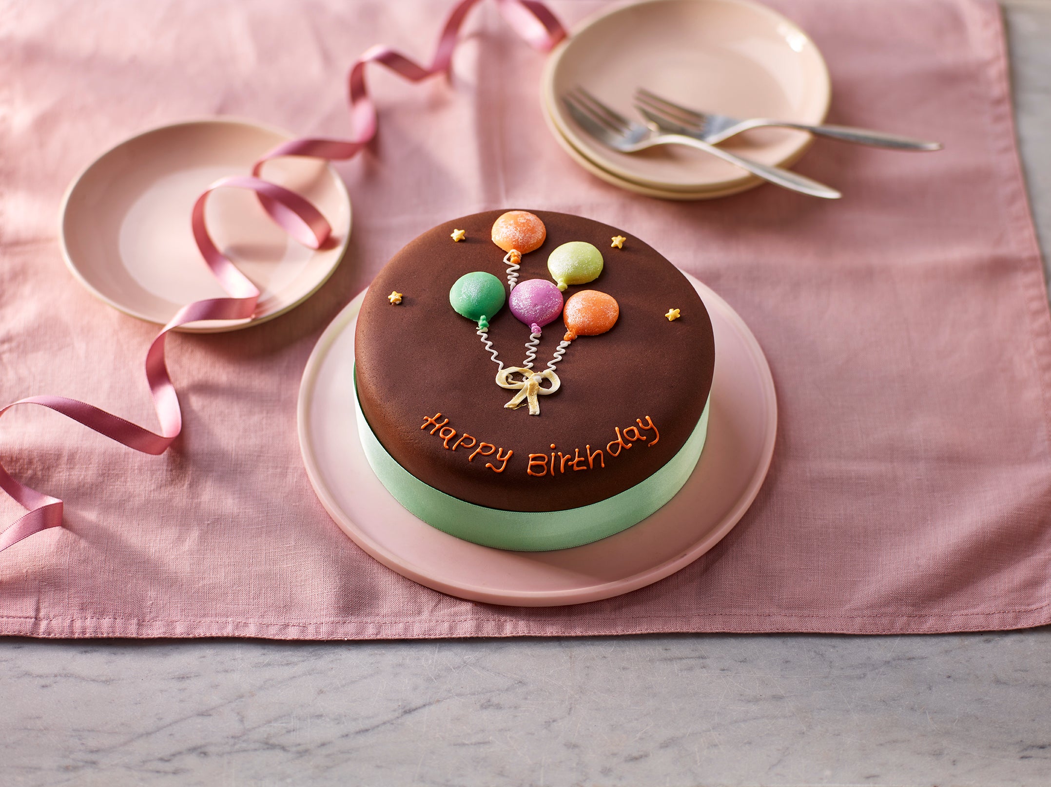 6-inch chocolate Happy Birthday cake with balloon decoration on a pink plate and ribbon background.