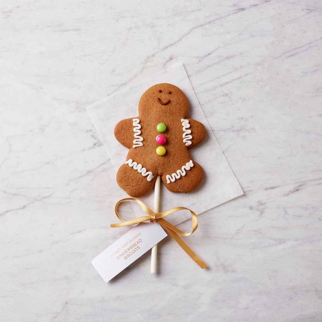 Gingerbread man lollipop decorated with icing and colourful buttons, tied with a gold ribbon and displayed on a marble background.