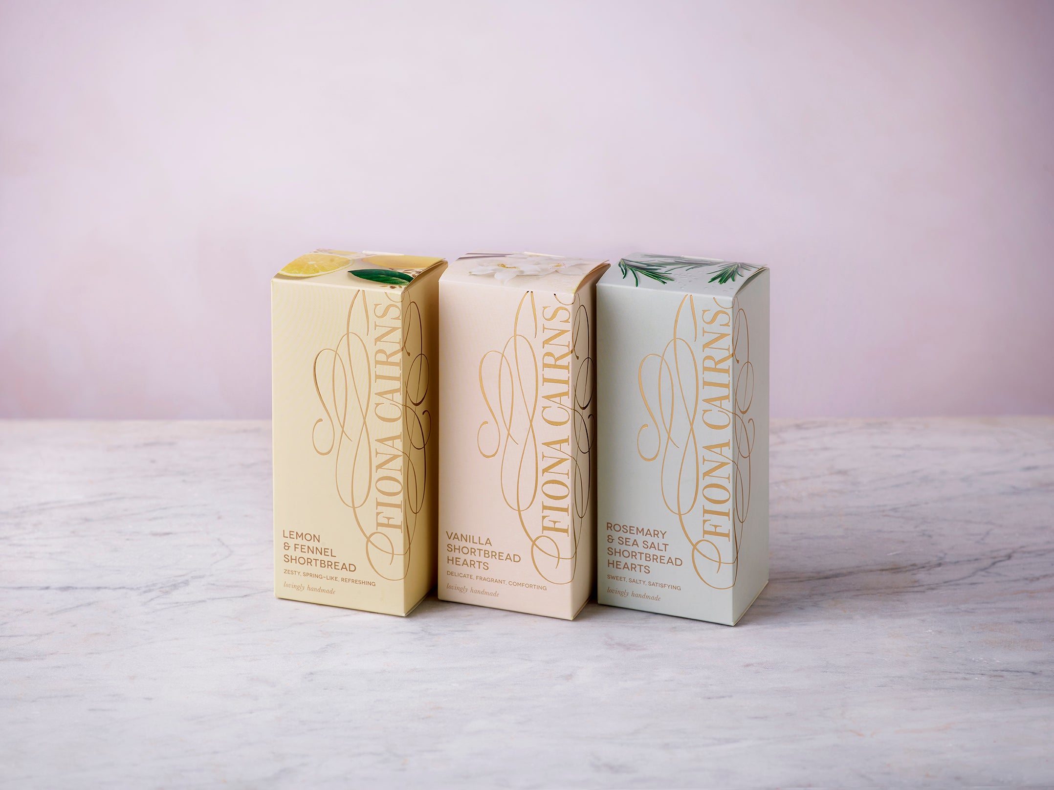 Biscuit and teatime treats bundle featuring three boxes of Fiona Cairns shortbread in pastel packaging, displayed on a marble surface with a soft pink background.