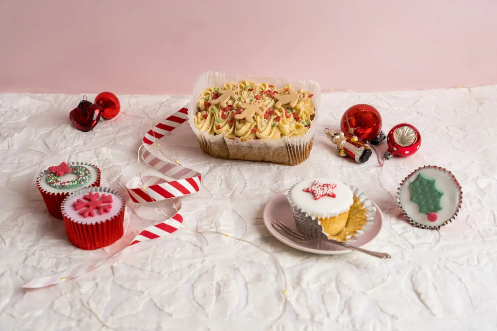 Gingerbread loaf cake topped with piped frosting, sprinkles and mini gingerbread men decorations, displayed on a white festive surface with Christmas ornaments.