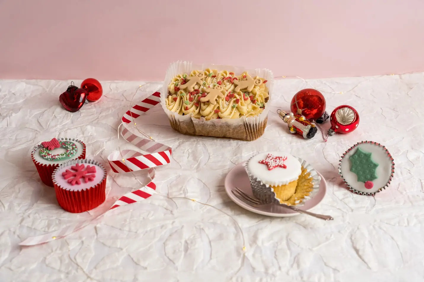 Gingerbread loaf cake topped with piped frosting, sprinkles and mini gingerbread men decorations, displayed on a white festive surface with Christmas ornaments.