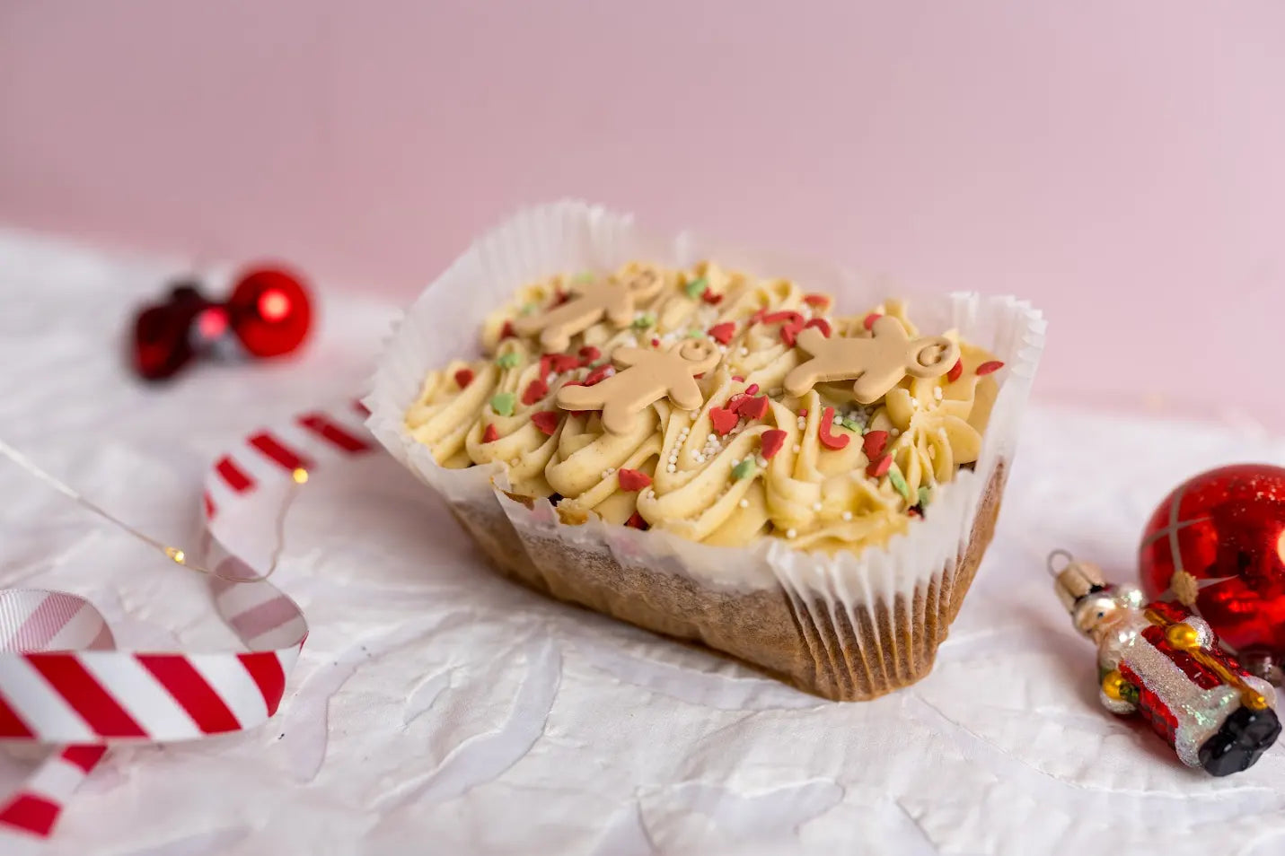 Gingerbread loaf cake topped with piped frosting, sprinkles and mini gingerbread men decorations, displayed on a white festive surface with Christmas ornaments.