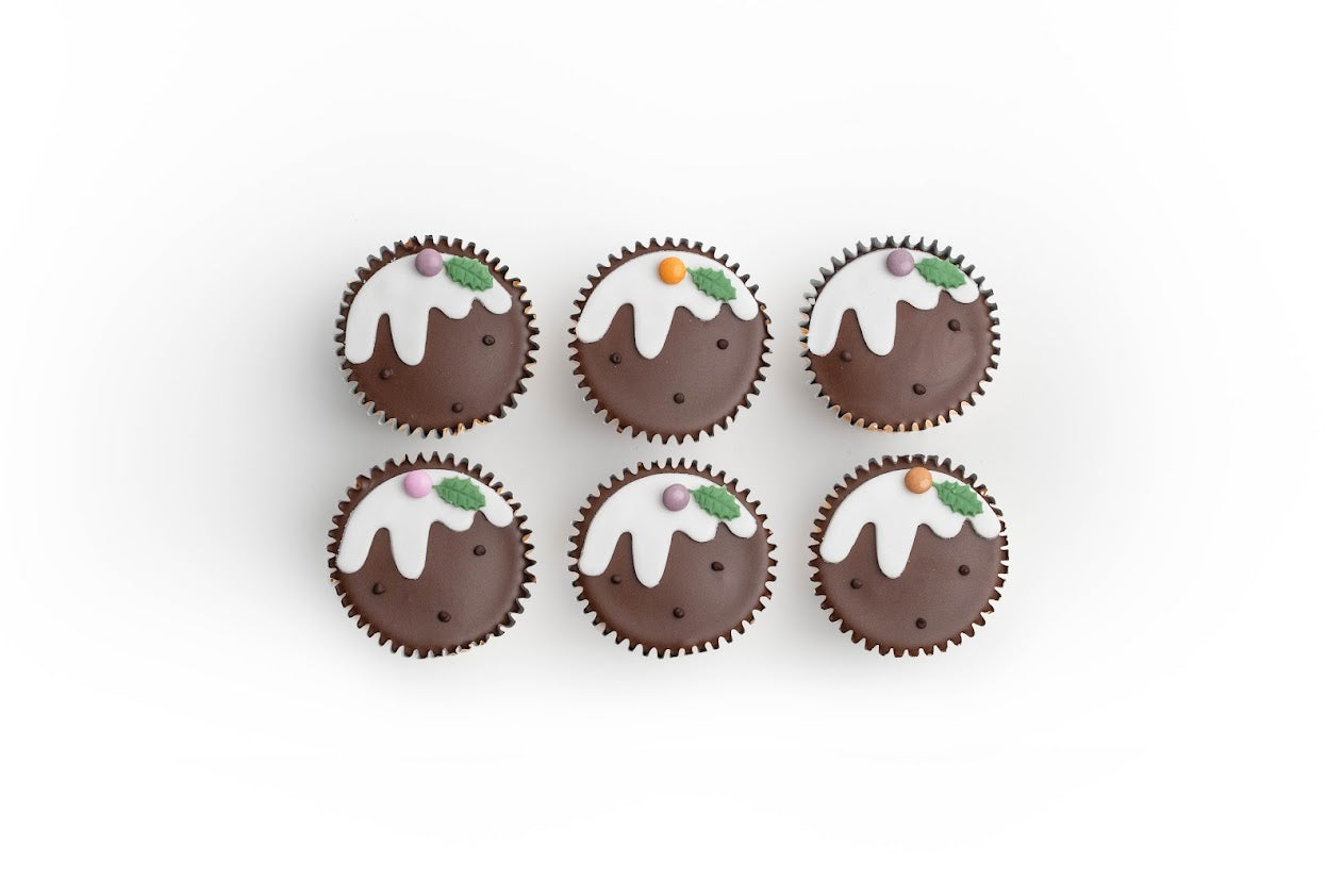 Six Christmas pudding fairy cakes with white icing and holly decorations arranged in two rows on a white background.